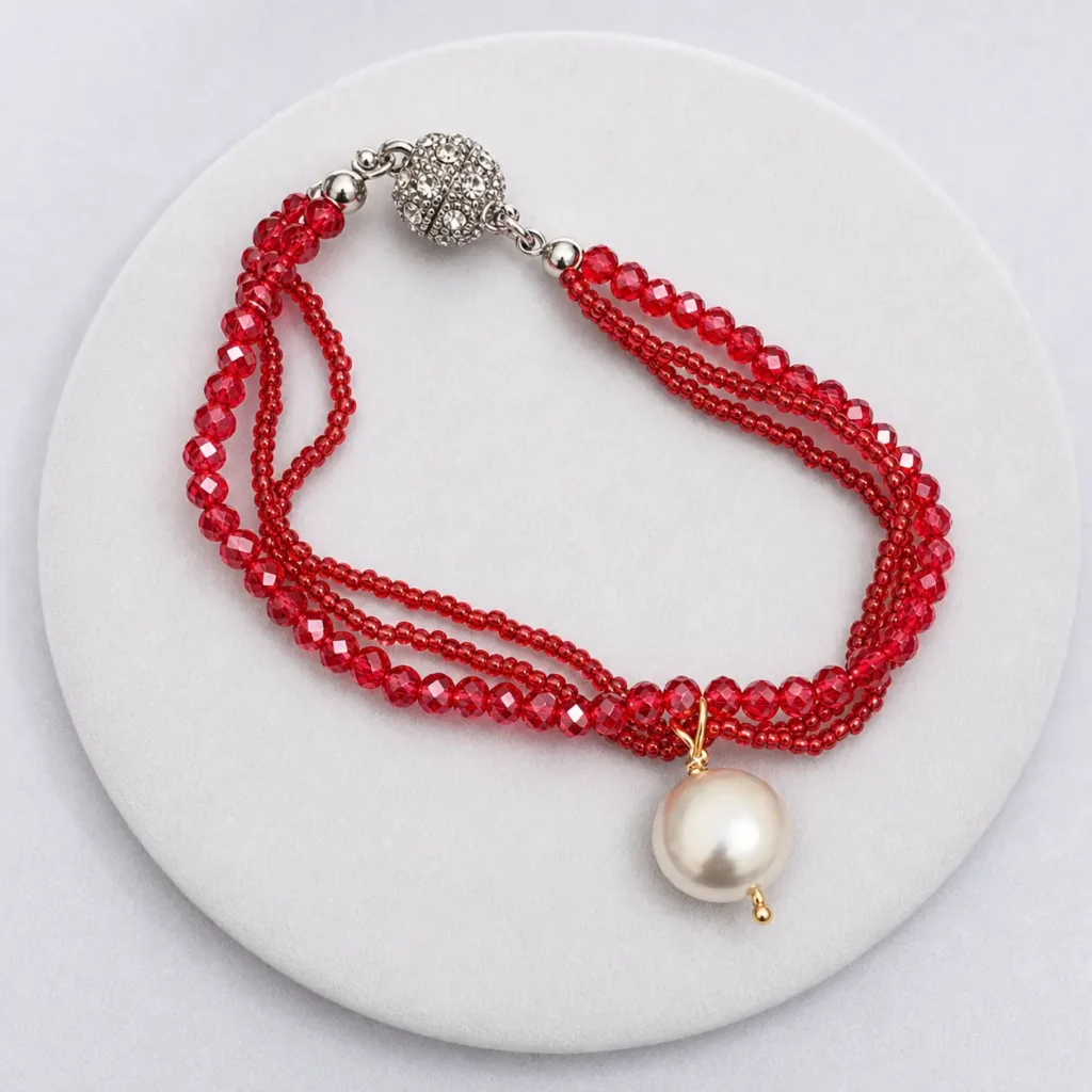 Bracciale multifilo con cristalli rossi sfaccettati, perla bianca pendente e chiusura magnetica con strass