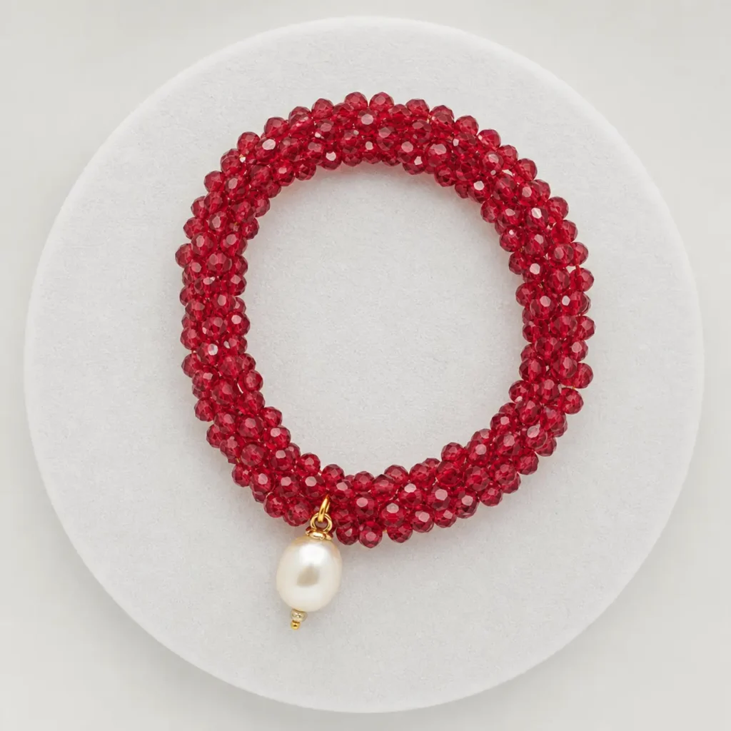 Bracciale a fascia intrecciata in cristalli rossi sfaccettati con perla bianca pendente e montatura dorata